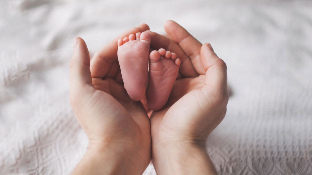 L'immagine mostra le mani di una mamma disposte a coppa che tengono i piedini di un neonato